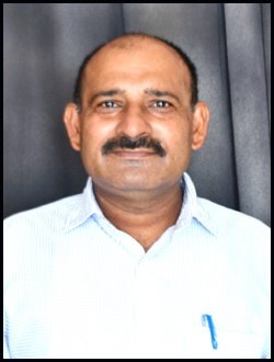 Portrait of Dr. Sharma wearing glasses and formal attire with academic background